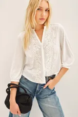 Camisa blanca de manga 3/4 con bordado de flores en el frente, cuello redondo y corte en V.
