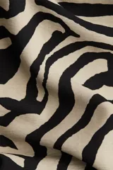 Pantalón amplio de sarga con estampado de cebra en tonos beige y negro, tiro alto, bolsillos al bies y cierre con botón y corchete ocultos.