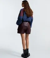 Short pollera corto color verde militar, confeccionado en poliuretano (PU) que imita el cuero. Presenta bolsillos delanteros grandes con solapas, pasadores en la cintura y cierre de cremallera.