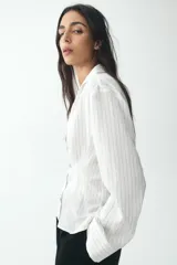 Camisa blanca con rayas verticales finas en color gris, de corte entallado, con cuello solapa y escote en pico. Cierre frontal con botones negros.