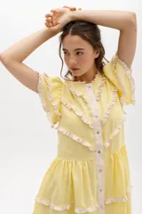 Vestido midi amarillo de lino, con volados en las mangas y detalle de volados y botones a lo largo del frente. Presenta un corte con talle marcado y falda escalonada.