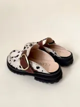 Zueco tipo mule negro, confeccionado en cuero vacuno, con puntera cuadrada y suela track gruesa. Presenta una faja ancha con hebilla metálica plateada sobre el empeine.