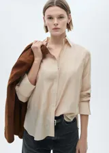 Camisa color beige claro de tejido satinado, con cuello camisero, manga larga con puños abotonados, corte recto y diseño oversize.