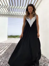 Vestido largo negro con escote en V y breteles finos. Presenta un aplique triangular de lentejuelas plateadas en la parte superior.
