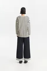 Jean ancho de tiro medio en denim oscuro, con bajos doblados que revelan un forro interior a rayas blancas y negras.