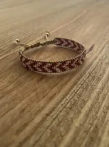 Pulsera tejida con cuentas originales MIYUKI en tonos de rojo oscuro y champagne, ajustable con cordón marrón claro.