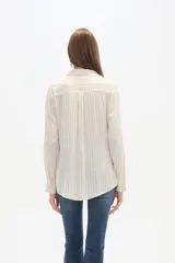 Camisa de viscosa color crema con finas rayas verticales negras, corte al cuerpo, cuello camisa y dos bolsillos frontales con tapa. Posee botones frontales y mangas largas con puño.