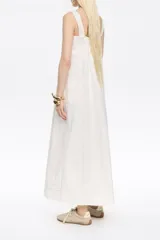 Vestido largo midi de corte línea A, color blanco, confeccionado en mezcla de lino. Presenta escote recto, tirantes anchos, fruncido en la espalda, bolsillos plastrón tipo alforja y pespuntes a contraste en toda la prenda.