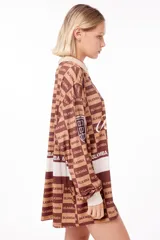 Camiseta oversize marrón con estampado de logos y texto "Blkmba" en toda la prenda. Tiene cuello en V con cuello tejido, escudo Mamba soccer en la manga y logo blkmba en el centro.