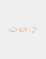 Set de tres anillos dorados con diferentes diseños: uno con strass, otro con detalle de color rosa y uno con una piedra transparente.
