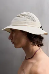 Sombrero tipo bucket color beige, confeccionado en tejido técnico con perforaciones en la copa para mejorar la transpirabilidad. Tiene ajuste elástico y ala ancha con pespuntes.