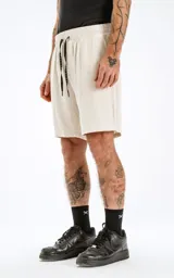 Bermuda color beige de algodón con elástico en la cintura, cordón bordado y bolsillos laterales.