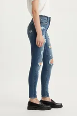 Jean skinny de tiro alto color azul denim con roturas grandes en ambas rodillas y pequeños detalles de roturas en los muslos.