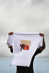 Remera blanca de manga corta con cuello redondo y estampado pequeño en el pecho de una figura humana caminando hacia una montaña.
