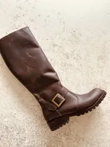 Bota de caña alta color marrón de cuero, con hebilla dorada y suela track.