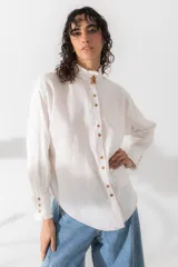Camisa blanca de lino con cuello mao con volados, cierre frontal con botones dorados y costuras en hilo naranja.