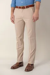 Pantalón de vestir color beige, de corte recto, con bolsillos laterales y traseros. Se ajusta a la cintura con cinturón de cuero marrón.