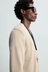 Jersey de punto color beige, con cuello en V y mangas largas.