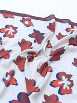 Pañuelo cuadrado de seda color crema con estampado de flores rojas, azules y blancas. Tiene borde marrón.