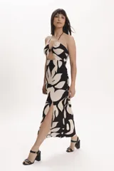 Vestido midi con estampado floral en tonos beige y negro, con escote halter, abertura en el abdomen y falda recta con tajo lateral.