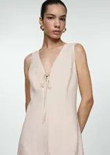 Vestido corto color beige de lino y viscosa, con escote en V y lazo decorativo en el centro.