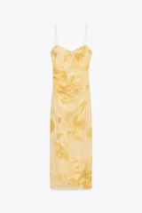 Vestido midi de tul color amarillo pálido con estampado floral, escote redondo y tirantes finos ajustables. Presenta detalle de frunces, forro interior y cierre lateral con cremallera oculta.