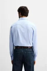 Camisa celeste de corte slim fit, confeccionada en tejido de algodón. Tiene cuello italiano, mangas largas con puños abotonados y cierre frontal con botones.