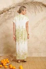 Vestido largo color blanco con estampado floral en tonos verdes y amarillos, con escote en V y mangas cortas.