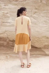 Vestido corto color mostaza con corte evasé y mangas cortas. Presenta un bloque de color marrón en la falda y otro bloque color beige en el ruedo.