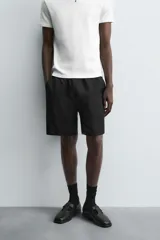 Bermuda negra de corte relajado, confeccionada en tejido satinado de viscosa. Presenta cintura elástica ajustable con cordón interior, bolsillos frontales y un bolsillo trasero de plastrón.