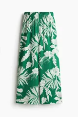 Pantalón ancho de punto con estampado floral blanco sobre fondo verde. Tiene tiro alto, cintura elástica y piernas amplias.
