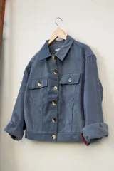 Campera azul de pana con cuello clásico, cierre frontal con botones dorados, bolsillos con solapa en el pecho y mangas largas con puños arremangados.