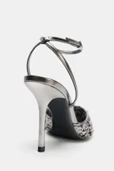 Zapato de tacón destalonado plateado con lentejuelas negras, tira al tobillo metalizada y punta fina.
