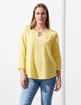Blusa blanca de tejido labrado con cuello redondo, escote en V y aplique metálico.