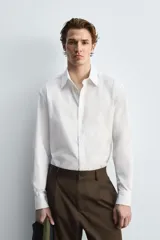 Camisa celeste de algodón con estructura twill, corte regular, cuello solapa, manga larga con puños abotonados y cierre frontal con botones.