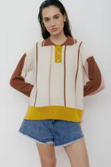Sweater de punto color crudo con rayas verticales marrones y rosadas, mangas largas color marrón y puños rosados, cuello polo marrón con botones amarillos y ruedo amarillo.