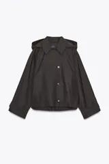 Trench corto color negro, con cuello solapa y capucha desmontable mediante botones. Manga larga tipo murciélago acabada en trabilla ajustable. Bolsillos laterales. Forro interior combinado. Cierre frontal con botones. Tejido repelente al agua.