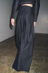 Pantalón de jean azul oscuro, de tiro muy alto y pierna ancha. Presenta pinzas en la parte delantera y cierre trasero con cremallera oculta.