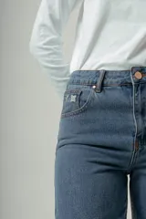 Pantalón de denim azul claro, tiro alto, de corte recto y pierna ancha. Presenta detalles bordados en el área de los bolsillos delanteros y traseros.
