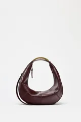 Bolso de mano ovalado color marrón oscuro, con asa de hombro metálica dorada y cierre superior con cremallera.