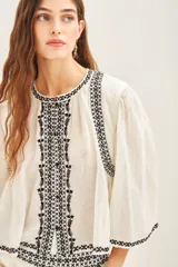 Camisa blanca de algodón con bordado negro en el ruedo, corte amplio y largo corto. Escote redondo y mangas largas abullonadas.