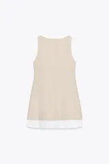 Vestido corto color beige, de cuello barco y sin mangas. Presenta un corte a la altura de la cadera y falda con tablas plisadas en color blanco.
