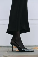 Zapato destalonado negro acharolado con tacón fino y punta. Tiene una tira trasera con elástico.