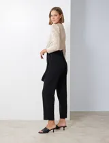 Enterito de fiesta con torso de lentejuelas color champagne, escote en V cruzado, mangas 3/4 con frunces en los hombros, cintura elastizada con lazo negro y pantalón negro de corte recto con bolsillos laterales.