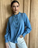 Camisa a rayas verticales color beige y blanco, de corte holgado, con cuello con volados, cierre parcial con botones y mangas largas con puños abotonados.