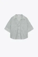 Camisa a rayas verticales grises y blancas, confeccionada en hilatura con lino, de cuello solapa y escote pico. Manga corta con trabilla y botón. Bajo asimétrico. Cierre frontal con botón.