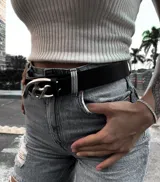 Cinto negro de cuero con hebilla metálica plateada con diseño abstracto.