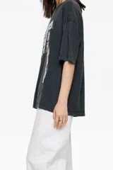 Camiseta blanca de algodón orgánico, corte oversize, con escote redondo y mangas cortas anchas. Presenta un logo grande en relieve en el frente.