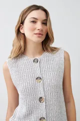 Chaleco tejido gris con botones de madera, sin mangas y cuello redondo.