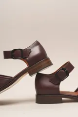 Zapato marrón de cuero vacuno trenzado a mano, con correa al tobillo con hebilla negra y suela de cuero.